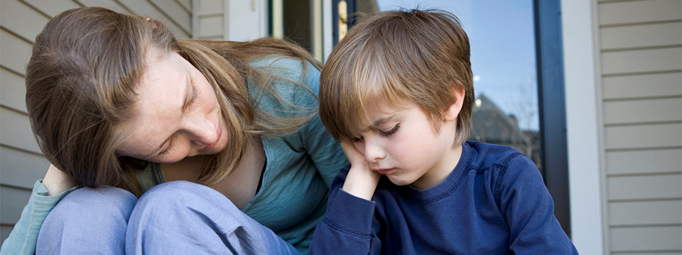 Photo of a mother sitting on the porch steps consoling her young son who appears to be sad.