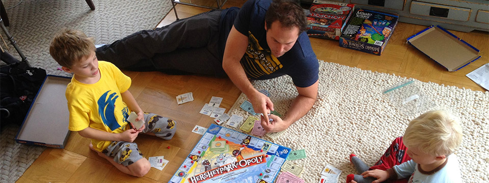 Photo of a father playing the Monopoly board game with his two sons.