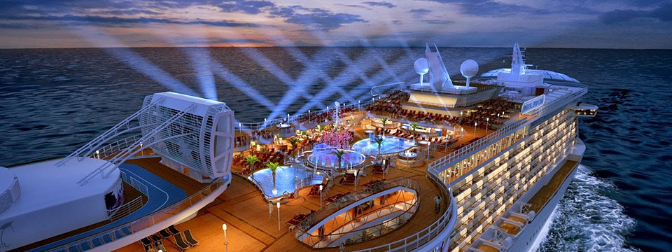 Photo of an aerial view of a beautiful luxury cruise ship at dusk. A beautiful array of criss-crossed spotlights shoot into the sky from the top deck.