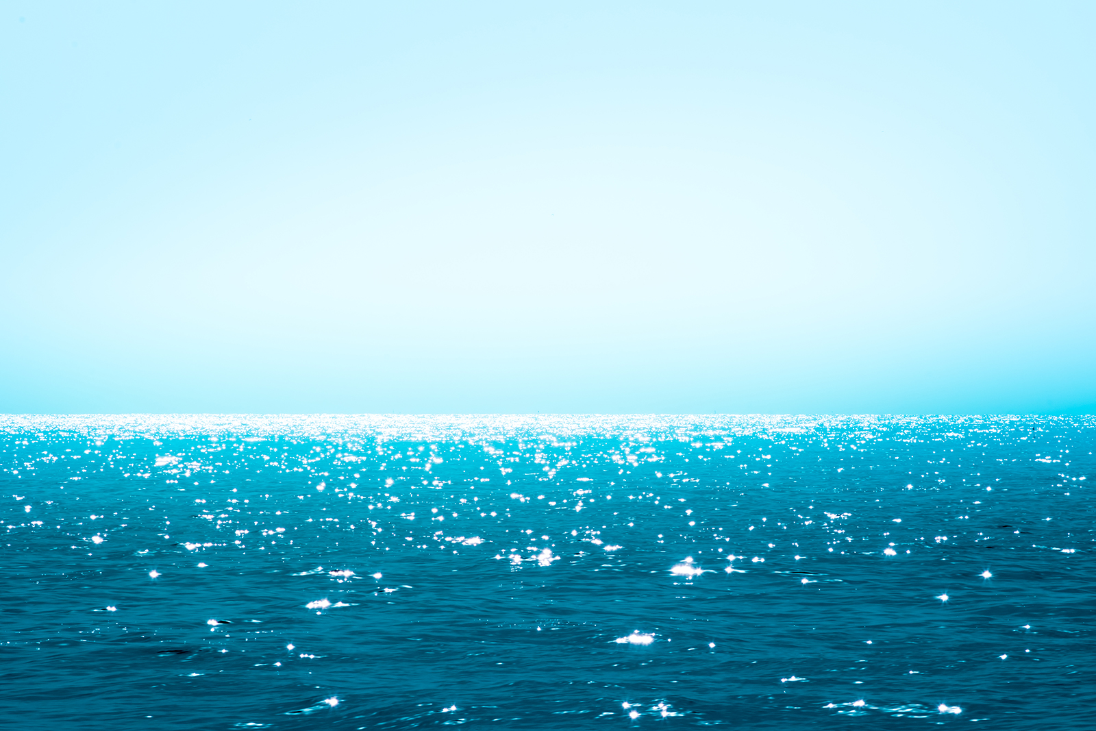 Image. A beautiful deep blue-green ocean sparkles in the sun for as far as the eye can see.
