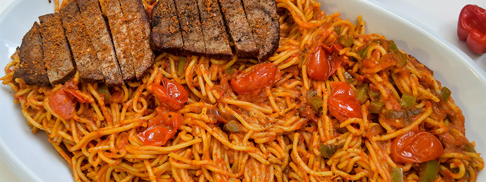 Photo of a beautiful plate of Jollof spaghetti with pan seared steak.