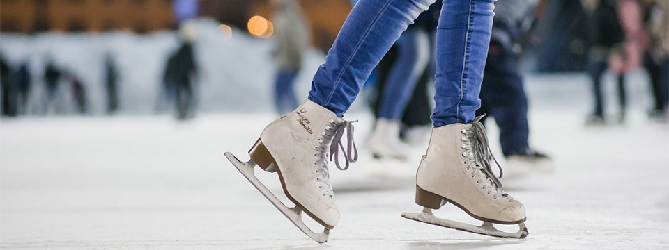 Close up of a girl wearing white ice skates and skating around an ice rink with everyone else blurred in the background.