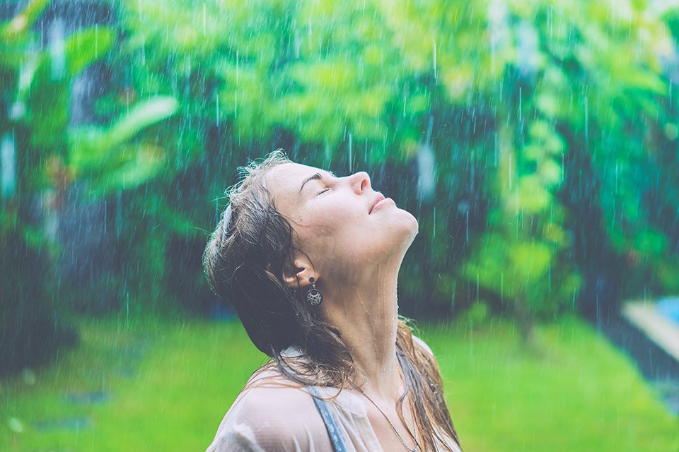 A girl stands outside in the April rain with her eyes closed and her face to the sky.