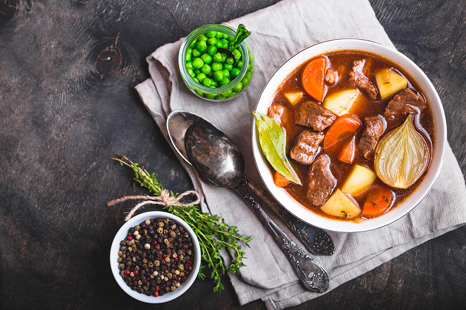 Meat stew with beef, potato, carrot, onion, spices. Green peas. Slow cooked meat stew in bowl, wooden background. Hot autumn/winter dish. Comfort food. Homemade soup/stew.
