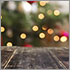 A beautiful thought-provoking photograph looks out across a worn wooden table. In the distance, slightly blurred, is the silhouette of a Christmas Tree full of decorations and lights.