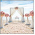 A beautiful dream-like wedding scene on a beach. No one in attendance. Lace and flower bouquets line a sand isle covered in rose petals. The ocean lies just beyond the altar.