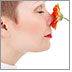 A woman holds a flower to her nose with her eyes closed and inhales deeply.